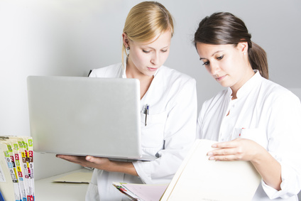 Zwei Damen lesen eine Krankenakte und schreiben in einen Laptop